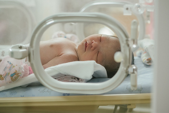 Premature upper body and head seen through hospital incubator